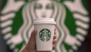 CHENGDU, SICHUAN PROVINCE, CHINA - 2015/09/13: Hand holding a cup of coffee in front of Starbucks logo. Starbucks is streamlining the ordering process so customers are able to get that cup of coffee  faster than usual. (Photo by Zhang Peng/LightRocket via Getty Images)